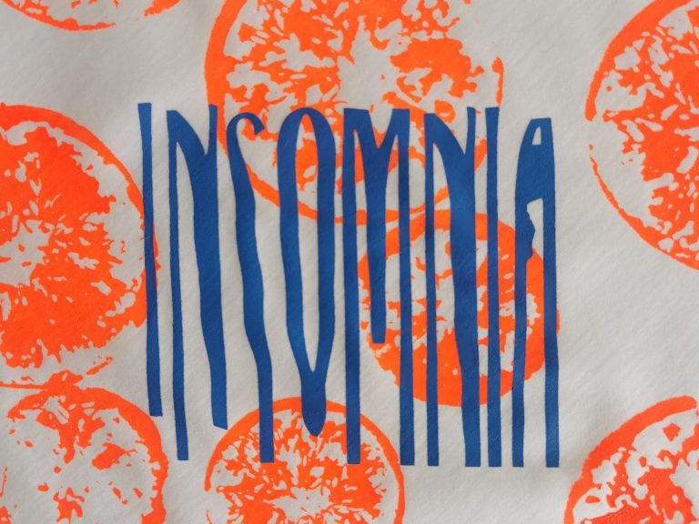 Insomnia Schriftzug auf Print Der Schriftzug "INSOMNIA" in blauen Buchstaben auf buntem Hintergrund mit Orangenmustern.
