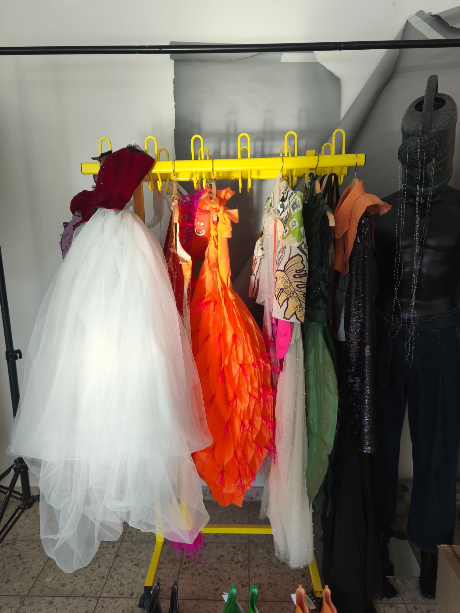 Shooting_BTS Bunte Kleidungsstücke hängen auf einem gelben Kleiderständer.